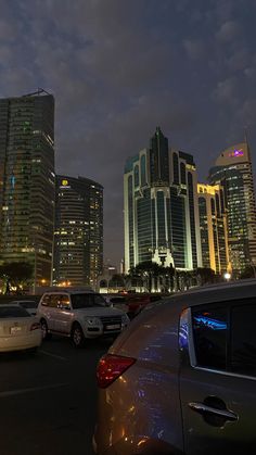 many cars are parked in a parking lot at night with skyscrapers in the background