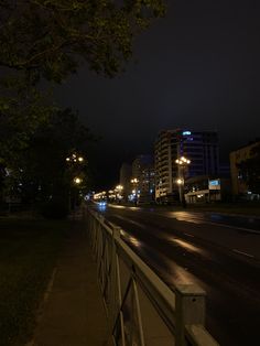 an empty city street at night with buildings in the background and lights shining on the road