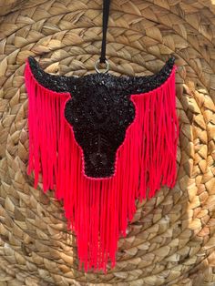 a black and red cow head hanging from a straw basket with pink fringes on it