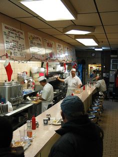 some people are in the kitchen preparing food and drinking beer while others wait for their order