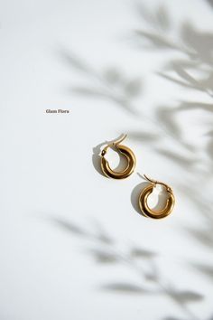 a pair of gold hoop earrings sitting on top of a white surface with shadow from the sun