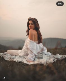 a woman sitting on top of a blanket in the middle of a grass covered field