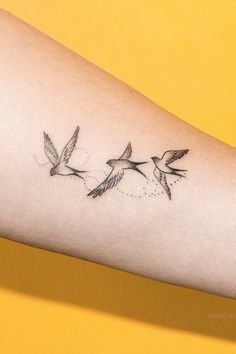 a tattoo on the arm of a woman with three birds flying above her and one is black