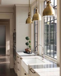 a kitchen with white cabinets and gold pendant lights hanging over the counter top, along with two sinks