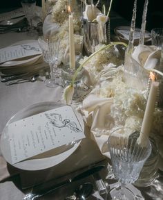 the table is set with white flowers, candles and menus for an elegant dinner