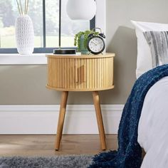 a nightstand with a clock on it in front of a window and a rug next to it