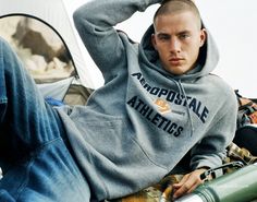 a young man sitting on the ground with his hands behind his head wearing a hoodie