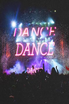 the words dance are lit up in front of an audience at a music festival with fireworks