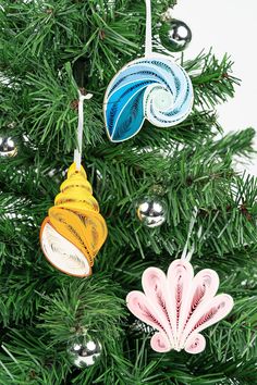 three ornaments are hanging from a christmas tree together, one is colorful and the other has an ornament shaped like a shell