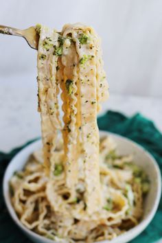 a spoon full of noodles with broccoli and cheese on it, being lifted from the bowl