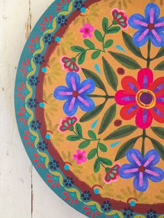 a painted plate with flowers on it sitting on a wooden table next to a wall