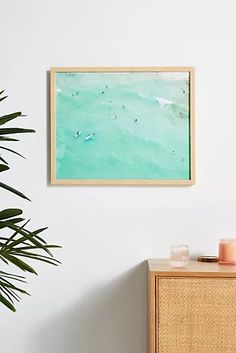 a painting hanging on the wall next to a wooden dresser and potted palm tree