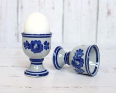 an egg sitting in a blue and white cup next to another one on a table