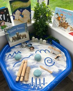 a blue table topped with toys and books on top of a window sill next to a potted plant