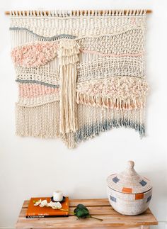 a woven wall hanging with tassels on it and a basket next to it