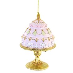 a pink and gold cake sitting on top of a golden stand with a chain hanging from it's side