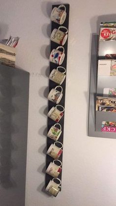 a shelf with cups hanging on it next to a mirror and wall mounted magazine rack