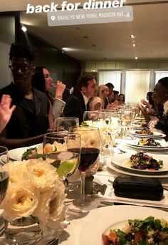 a group of people sitting at a table with food and wine glasses on top of it