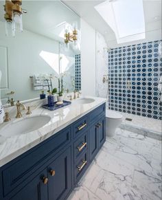 a bathroom with blue cabinets and marble counter tops, along with a skylight above the sink