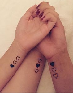 two girls with matching tattoos on their arms holding hands and looking at each other's wrist