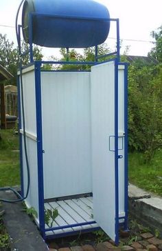 a blue and white toilet sitting on top of a brick walk - in shower next to a lush green yard