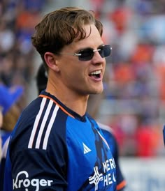 a young man wearing sunglasses standing in front of a crowd at a soccer game with an excited look on his face