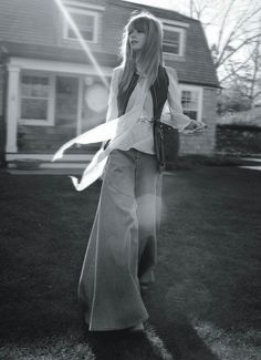 black and white photograph of woman in front of house with long hair wearing wide pants