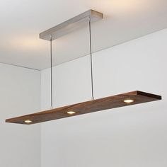 a suspended light fixture with three lights on the ceiling in a white walled room next to a window