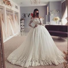 a woman standing in front of a mirror wearing a white wedding dress with long sleeves