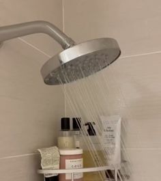 a shower head with soap, shampoo and lotion on the shelf next to it