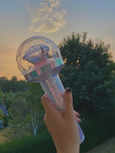 a hand holding up a plastic object in the air with trees and bushes behind it