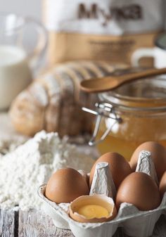 some eggs are in a carton on a table next to flour and other ingredients