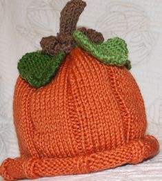 an orange knitted pumpkin hat sitting on top of a white bedding sheet,