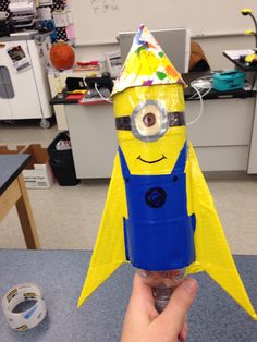 a hand holding up a paper model of a minion with a party hat on