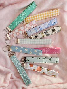 six keychains are lined up on a pink blanket with flowers and gingham