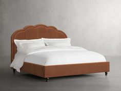 a bed that has a brown headboard and white sheets on it, with a light gray wall in the background