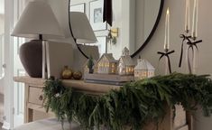 a mantle with christmas decorations and candles on it in front of a large round mirror