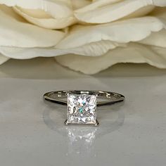 a close up of a diamond ring on a table with flowers in the back ground