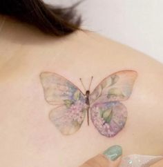 a butterfly tattoo on the back of a woman's left shoulder, with pink flowers and green leaves