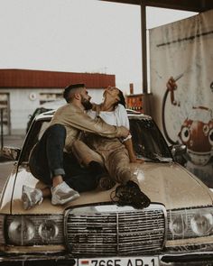 a man and woman sitting on top of a car in front of a gas station