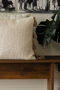 a wooden table topped with a pillow covered in tassels next to a plant