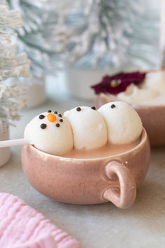 three little snowmen sitting in a cup with marshmallows on it and one is holding a spoon