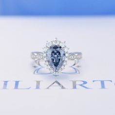 a blue and white diamond ring sitting on top of a piece of paper with the word illarto written below it