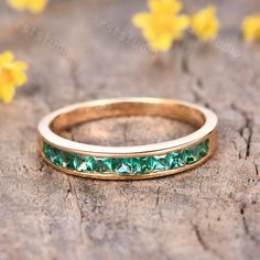 a gold ring with green stones on it sitting on a wooden surface next to yellow flowers