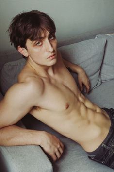 a shirtless man laying on top of a couch next to a wall and looking at the camera