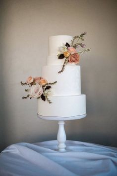 a three tiered white wedding cake with flowers on the top and bottom, sitting on a blue table cloth