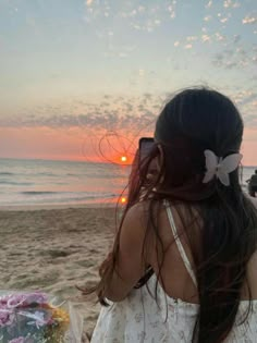 a woman sitting on top of a beach next to the ocean with her hair blowing in the wind