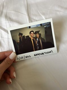 a person holding up a polaroid with an image of two graduates on it's back