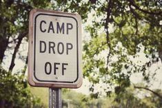 a sign that says camp drop off on the side of a pole in front of some trees