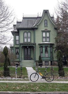 a bicycle is parked in front of a green victorian style house on a street corner